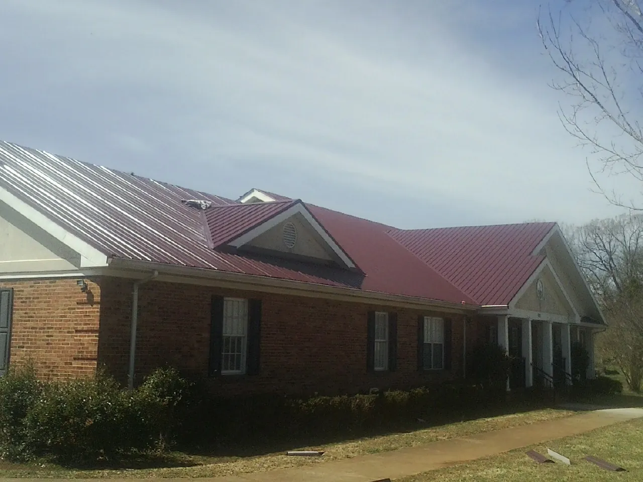 Red metal roof with gabled entries on a long brick building, from a Hail Damage Roof Repair job in Kingsbury