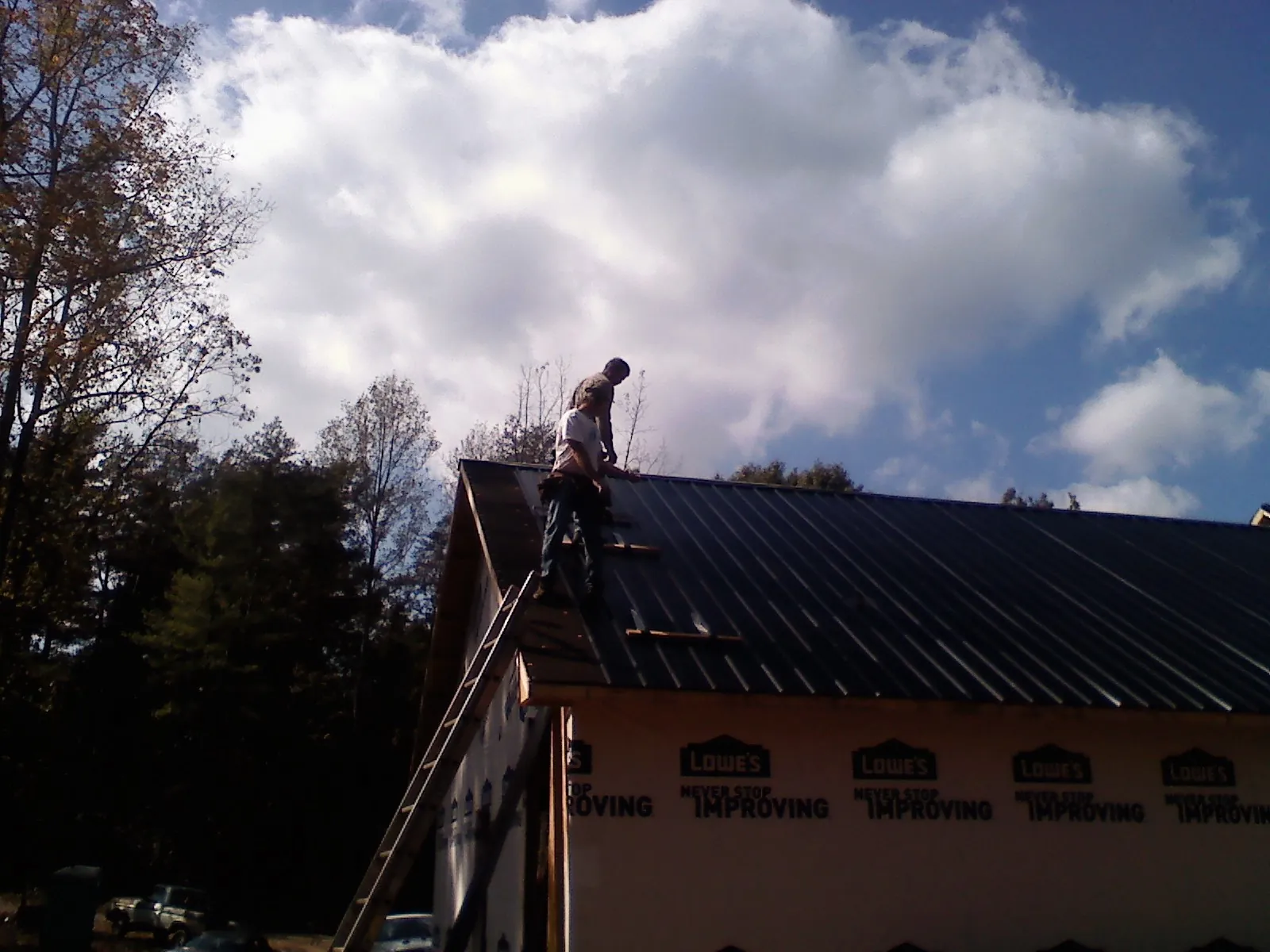 Roofer fastening dark metal panels high against a cloudy sky, from a Roof Inspection job in Kingsbury
