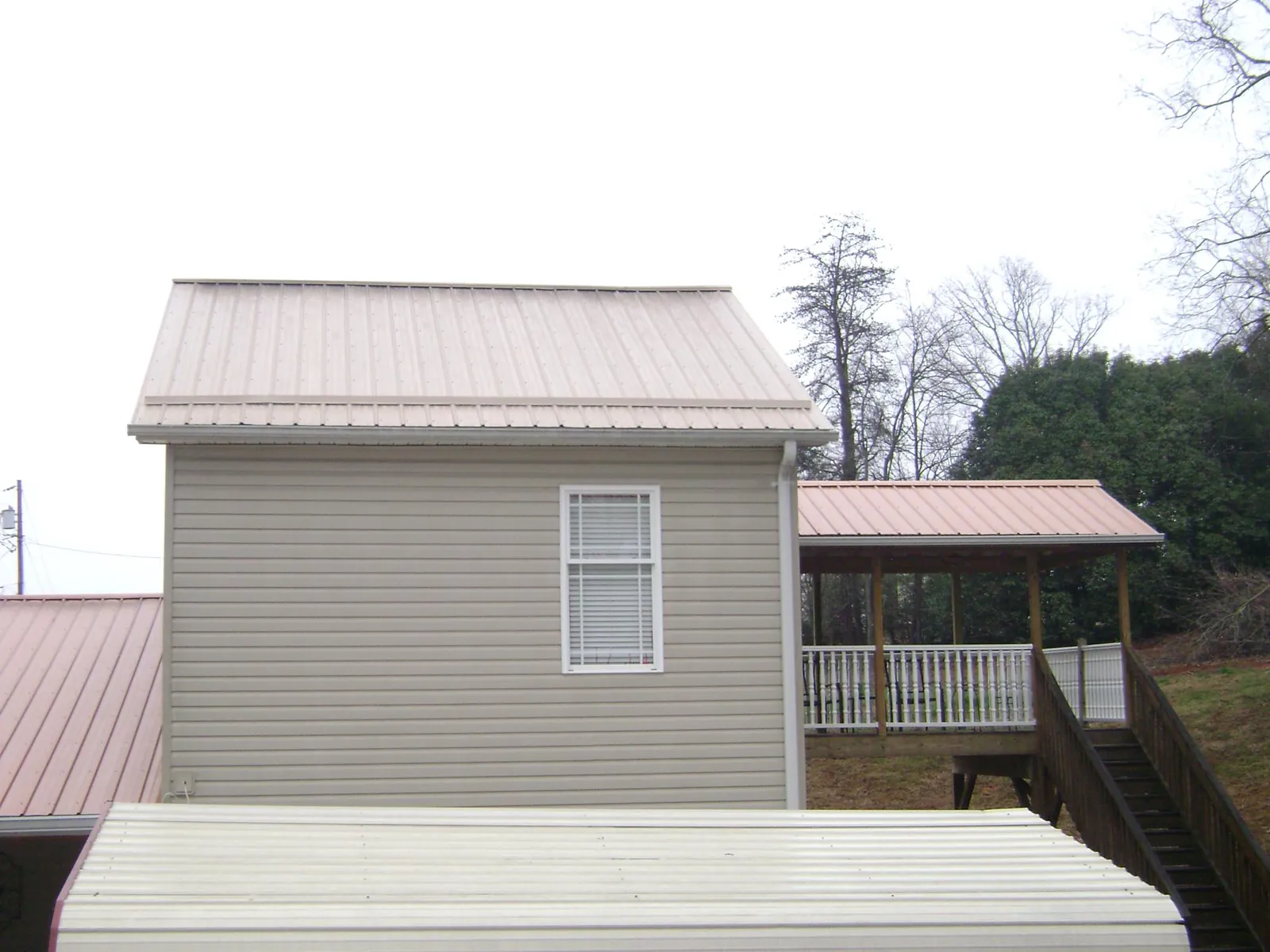 Tan metal roofs on a two story addition and attached porch, from a Roof Replacement job in Kingsbury